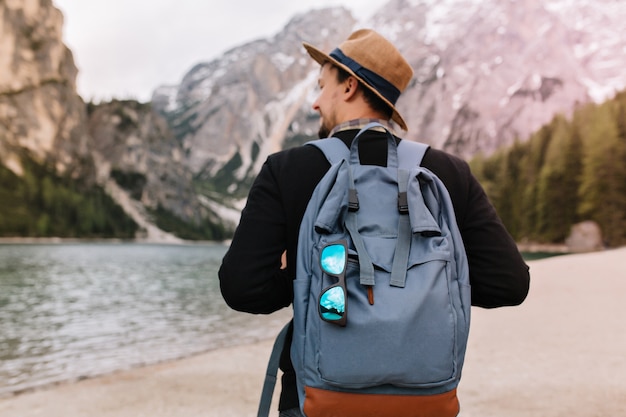 Free Photo outdoor portrait from back of male tourist carrying big decorated backpack and walking to mountains in morning