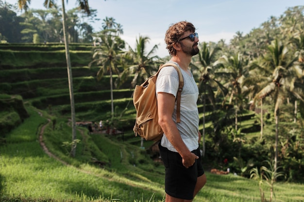 Outdoor portrait of Handsome travel man with back pack walking on rise terrace in Bali.