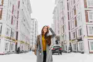 Free photo outdoor portrait of long-haired woman in trendy gray coat going to shopping in snowy day. gorgeous blonde woman in stylish outfit spending time in city in winter weekend.