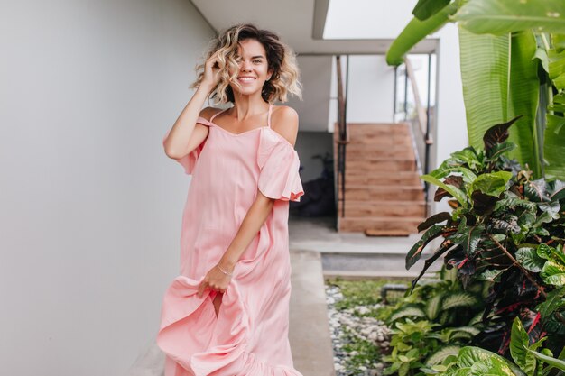 Outdoor portrait of trendy caucasian girl expressing positive emotions near stairs. Pleasant tanned female model in pink dress dancing with cheerful smile.