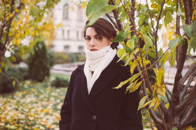 Outdoor portrait of woman in park wearing winter black coat and white scarf