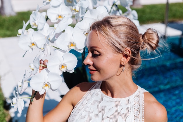 Free Photo outdoor portrait of woman in white wedding dress sitting near blue swimming pool with flowers