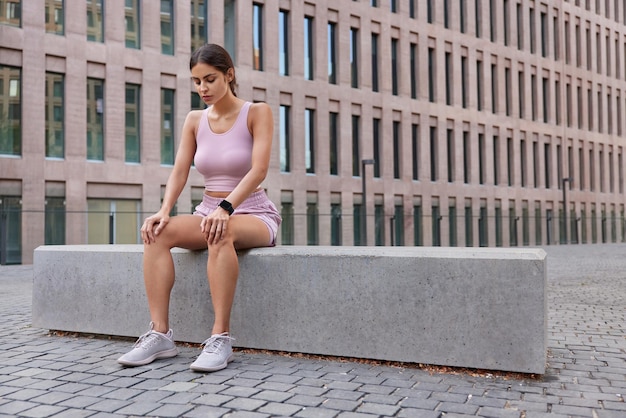 Free photo outdoor shot of active sporty woman rests in urban setting breathes deeply after workout wears sportsclothes and sneakers feels tired