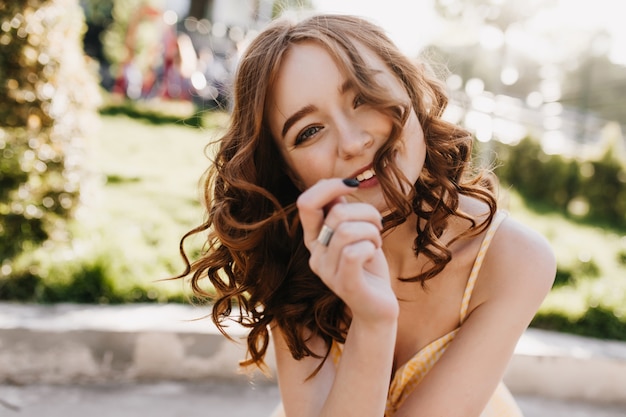 Free photo outdoor shot of attractive red-haired female model relaxing on nature. portrait of lovely ginger girl with wavy hairstyle.