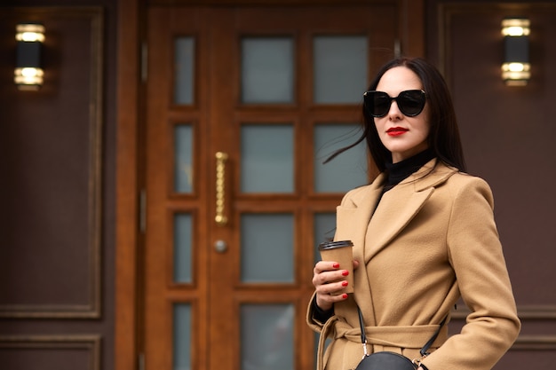 Outdoor shot of beautiful young stylish brunette woman wearing beige coat posing in open air