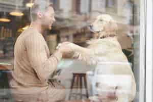 Free photo an outdoor shot of a man sitting with his dog in a petfriendly cafe near window golden retriever