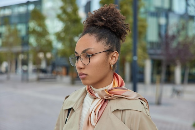 Free photo outdoor shot of serious intelligent female teacher wears round glasses and coat walks in city returns from work being deep in thoughts considers future plans