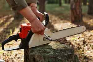 Free photo outdoor shot of unknown person worker fixing chainsaw before or after deforestation