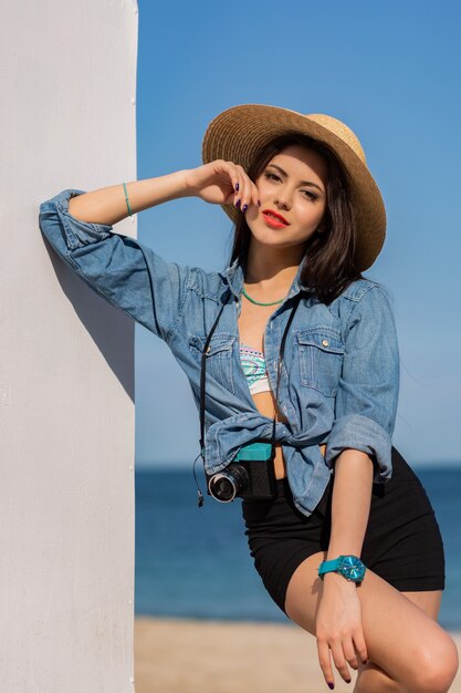 Outdoor summer fashion portrait of gorgeous woman with tan body, full red lips and long strong legs posing on the tropical sunny beach.