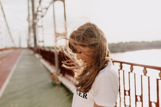 Outside portrait of of appealing girl smiling with wonderful happy emotions and covering face with flying hair