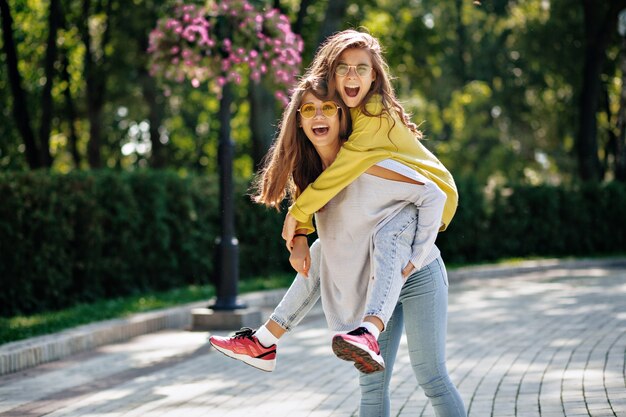 Outside portrait of two adorable ladies have fun joking and laughing together in the street, foolong, jumpimg, have a good mood in the city