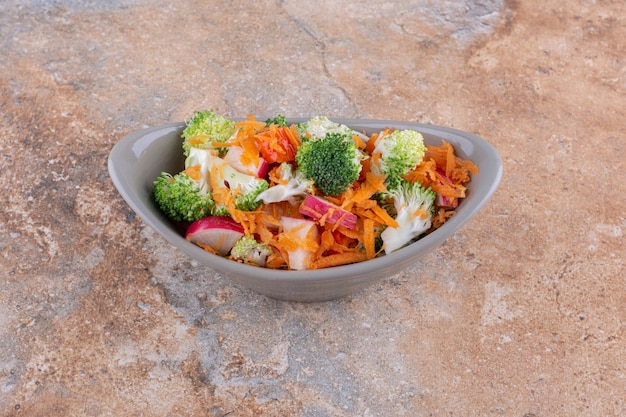 Oval bowl of mixed vegetable salad displayed on marble surface