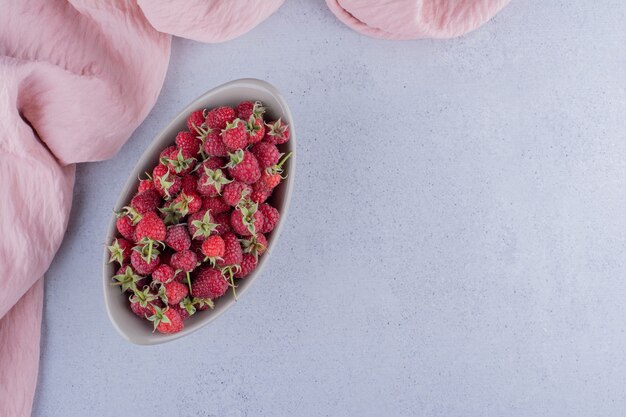 Oval bowl stocked with raspberries on marble background.