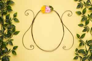 Free photo oval shape frame with artificial rose on yellow wall with green leaves