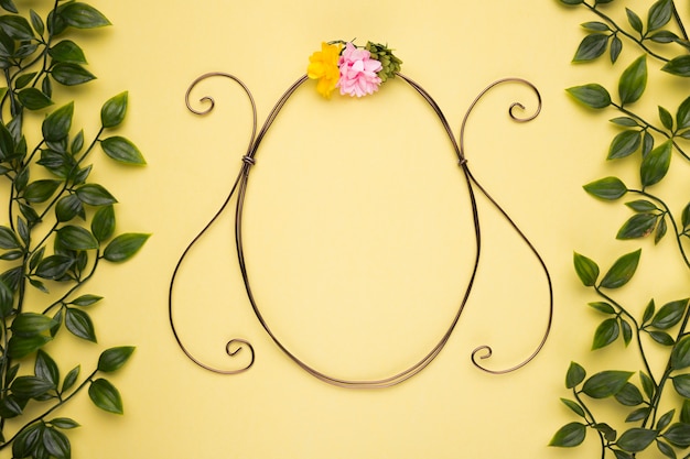 Free Photo oval shape frame with artificial rose on yellow wall with green leaves