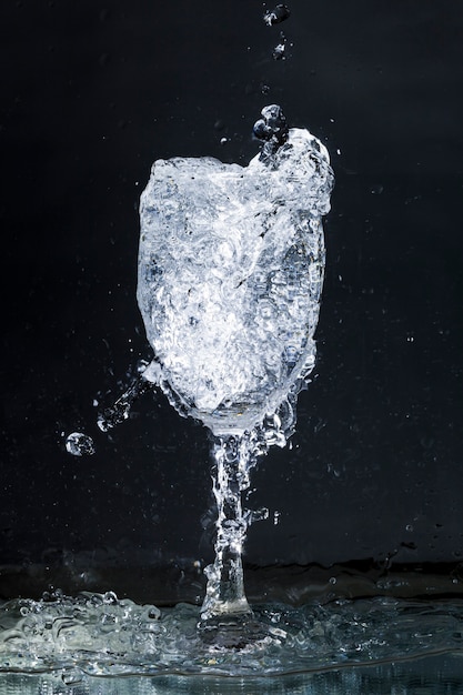 Overflowing water glass on dark background