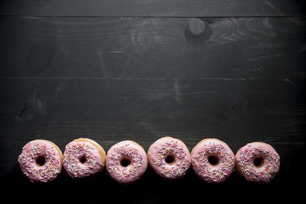 Free Photo overhead shot of a black wooden surface with pink donuts on the bottom great