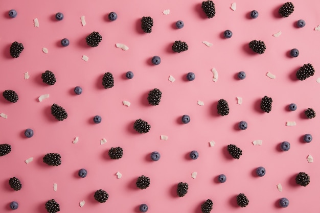 Overhead shot of juicy blueberry and blackberry, coconut flakes on rosy background. Summer time and nutrition concept. Healthy organic ripe seasonal berries for preparing dessert. Nutrient food