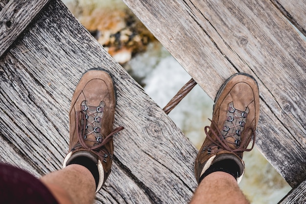 Free photo overhead shot of a male feet standing on a wooden bridge wearing hiking shoes