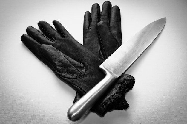 Free photo overhead shot of a metal knife over black gloves on a  white surface