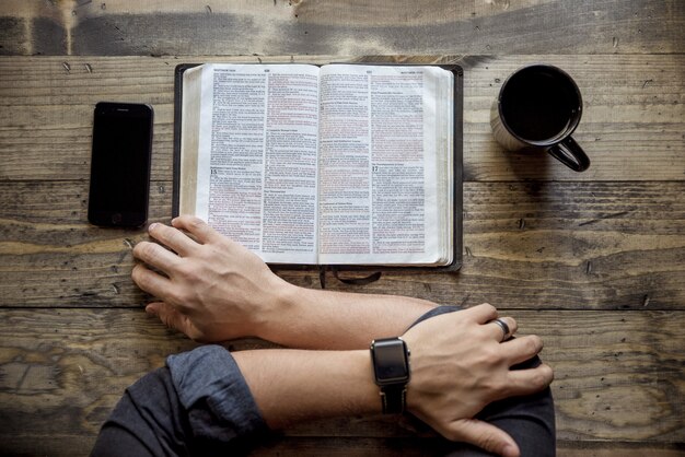 Overhead shot of a person reading a book near coffee and smartphone on the wooden table