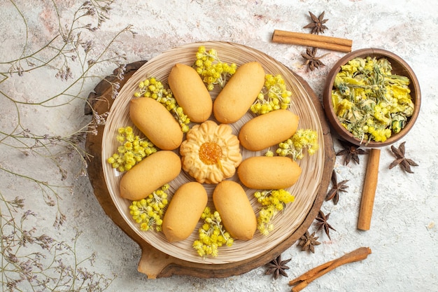 Overhead shot of a plate of cookies on wooden platter and diferent dried herbs on marble ground