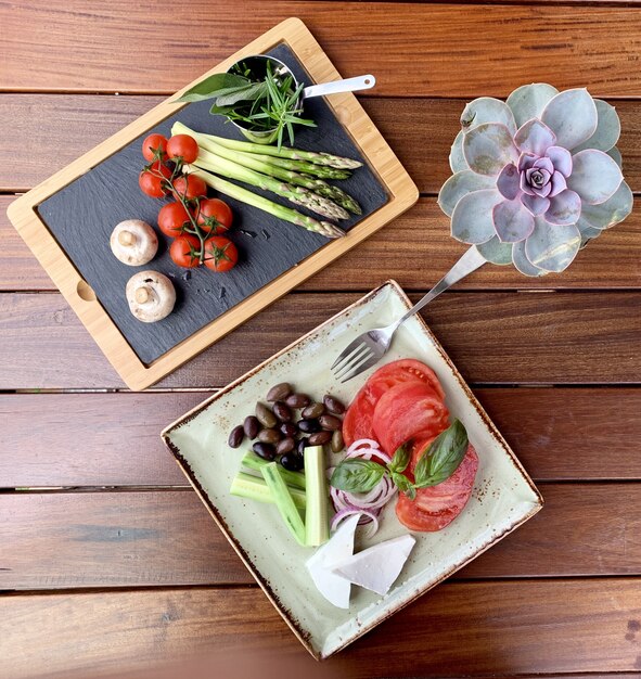 Overhead shot of salad with beans and cheese on a plate near a wooden tray with vegetable near  rose