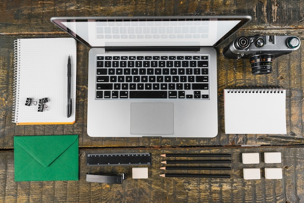 Overhead view of arranged office stationeries and laptop; retro camera on wooden desk