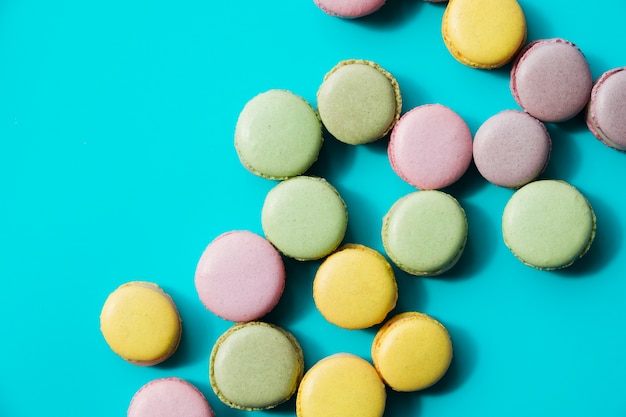 Free photo an overhead view of baked green; yellow and pink macaroons on blue background