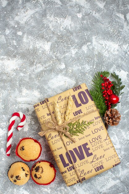 Overhead view of beautiful Christmas packed gift with love inscription small cupcakes candy and fir branches decoration accessories conifer cone on ice surface