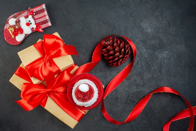 Overhead view of beautiful gifts with red ribbon and santa claus hat conifer cone christmas sock on dark table