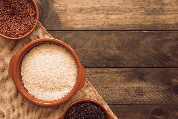 Overhead view of black; red and white organic rice grains on jute cloth over the wooden table