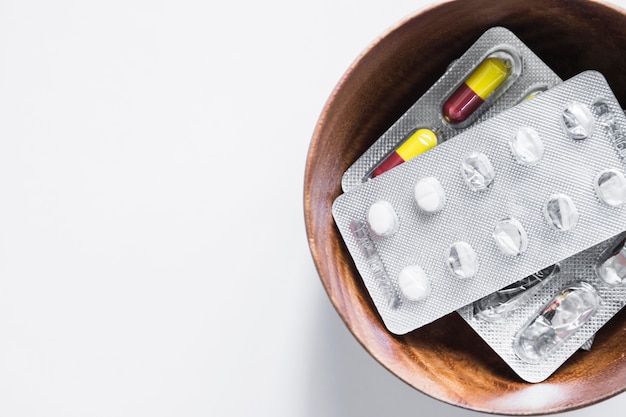 Overhead view of blister pack pills in bowl on white background