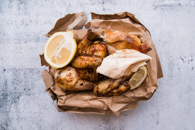 Overhead view of boiled and roasted chicken with lemon in brown paper over concrete background