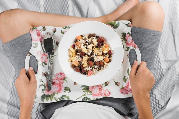 An overhead view of a boy holding floral tray with oat flakes and forest fruits