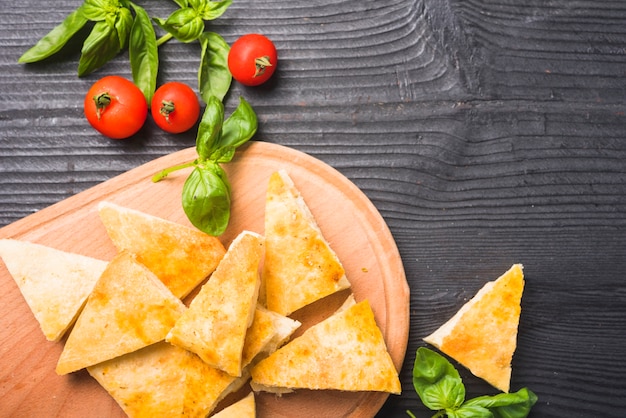 An overhead view of bread slices with basil leaves and tomatoes on wooden table