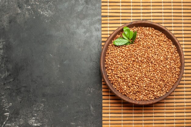 Overhead view of buckwheat groats with green in a brown bowl on brown tray on the left side on gray background