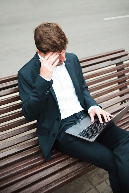 An overhead view of a businessman sitting on bench at street using laptop