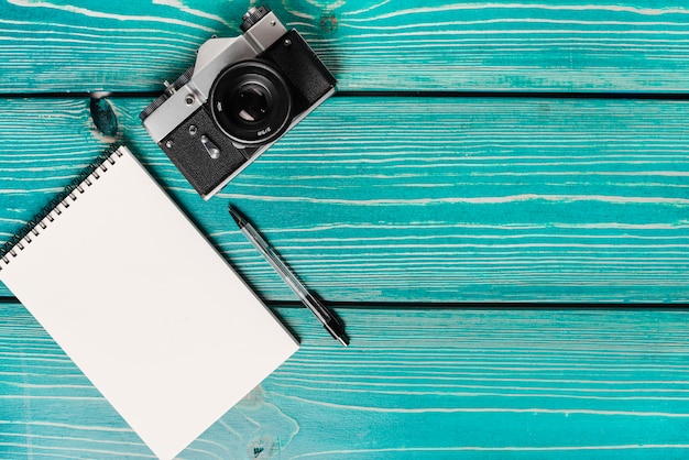 Free photo an overhead view of camera; spiral notepad and pen on wooden plank