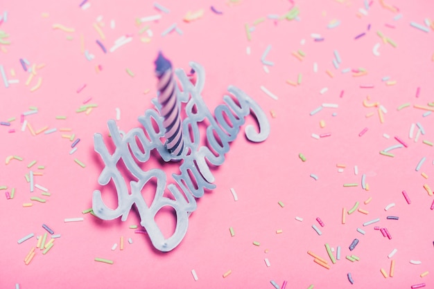 Free photo overhead view of candle over the happy birthday text and sprinkle on pink backdrop