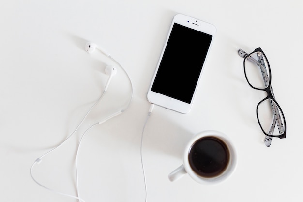 Free photo overhead view of cellphone with connected earphone, coffee cup and eyeglasses