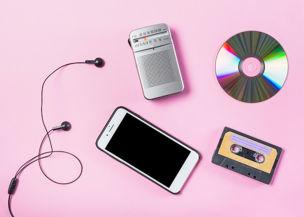 Free Photo an overhead view of cellphone with earphone; cd; radio and cassette on pink background