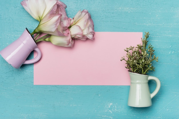 An overhead view of ceramic vases on pink blank paper on wooden blue background