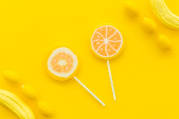 Overhead view of citrus lollipops; banana and lemon candies on yellow surface