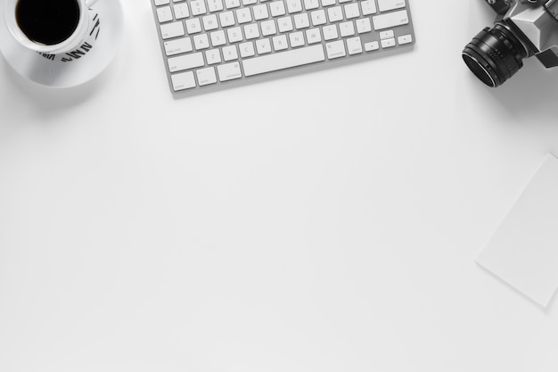 An overhead view of coffee cup; keyboard; camera and paper on white background