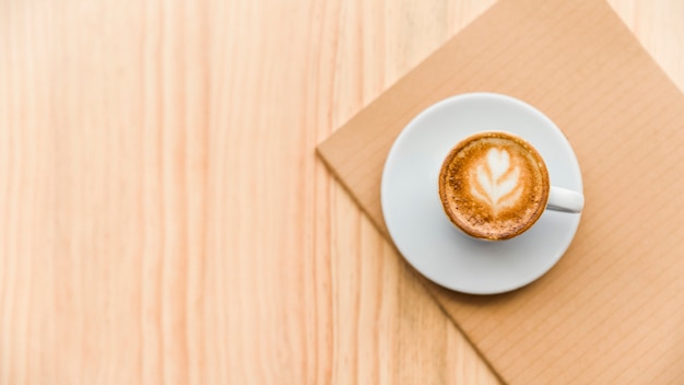 Overhead view of coffee latte and notebook on wooden backdrop