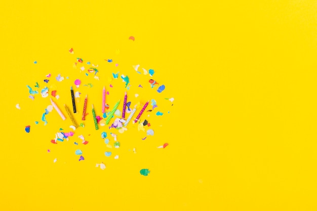 Overhead view of colorful candles with confetti on yellow background