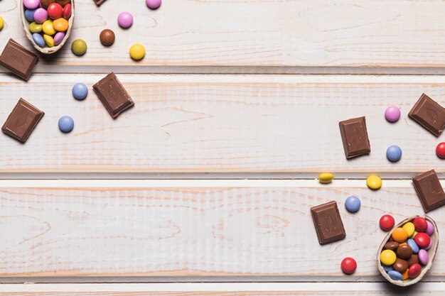 An overhead view of colorful gems and chocolate pieces on wooden desk