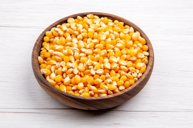 Overhead view of corn kernels in a brown bowl on white background