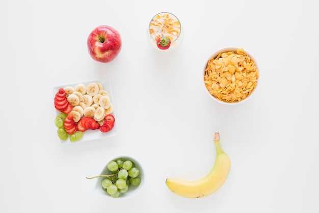 An overhead view of cornflakes with apple; banana; strawberry and grapes isolated on white backdrop